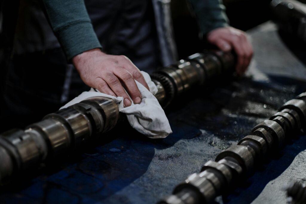 pexels-photo-7565174-7565174 Close-up of a mechanic cleaning a camshaft with a cloth in an industrial setting.
